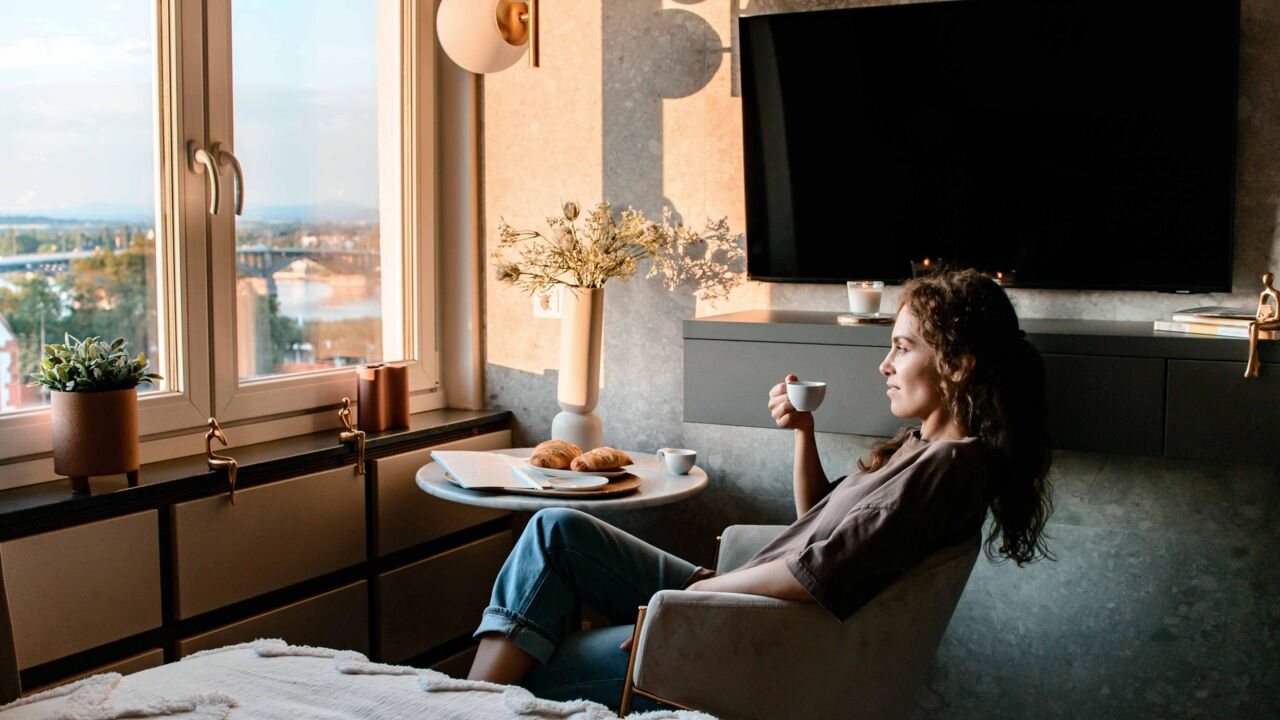 Frau sitzt in Ferienwohnung und genießt Ausblick mit Espresso in der Hand
