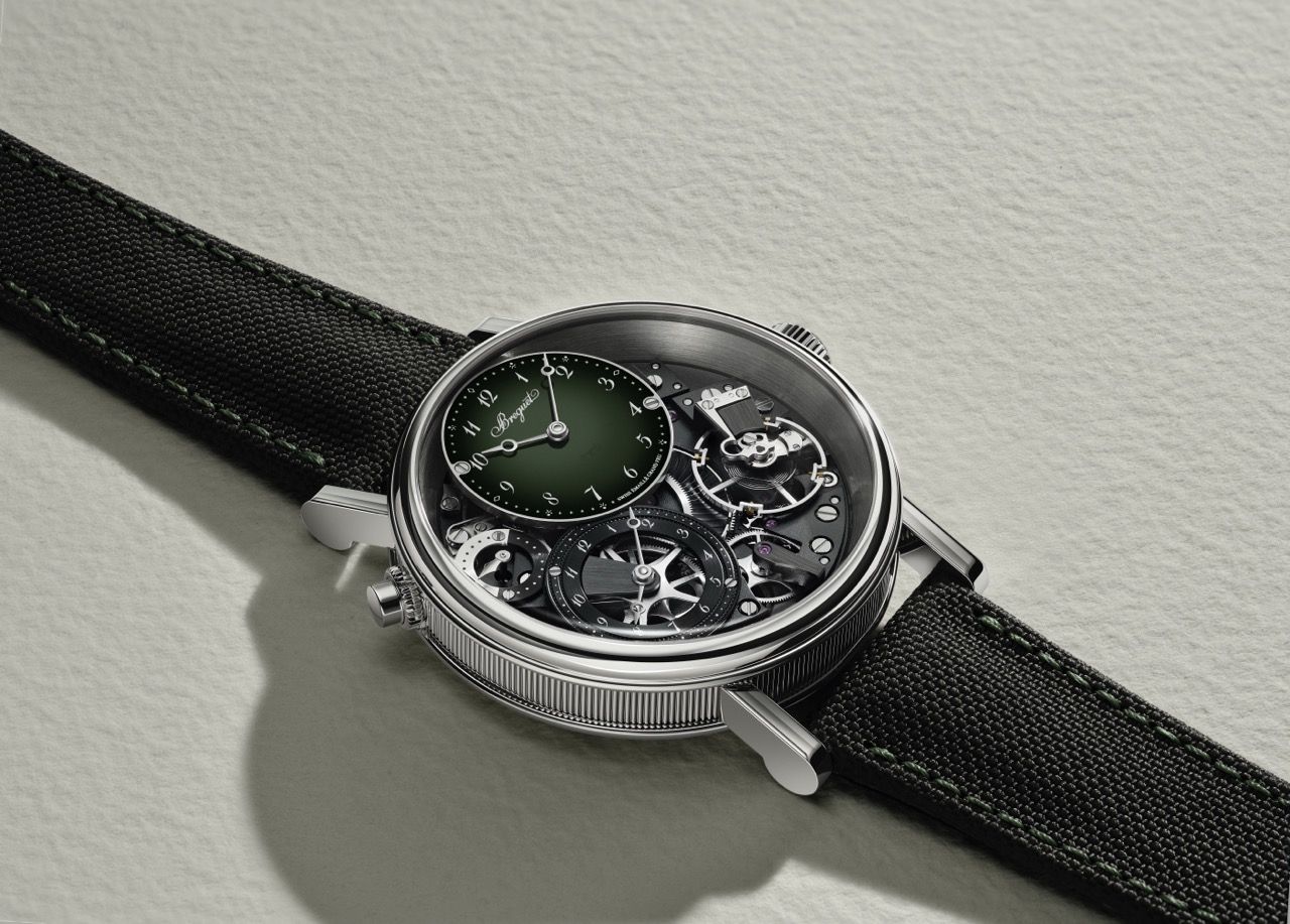Nahaufnahme der Platin-Luxusuhr Breguet Tradition GMT 7067PT mit offenliegendem Uhrwerk und einem versetzten, tannengrünen Zifferblatt mit Farbverlauf auf einem schwarzen Textilband.