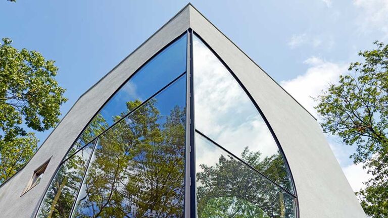 Schön verbunden: Vom Park aus betrachtet, spiegelt ein großes Rundfenster die umgebenden Bäume und den Himmel wider –  und sorgt für eine  Verbindung von Innen und Außenwelt . Großes Rundfenster