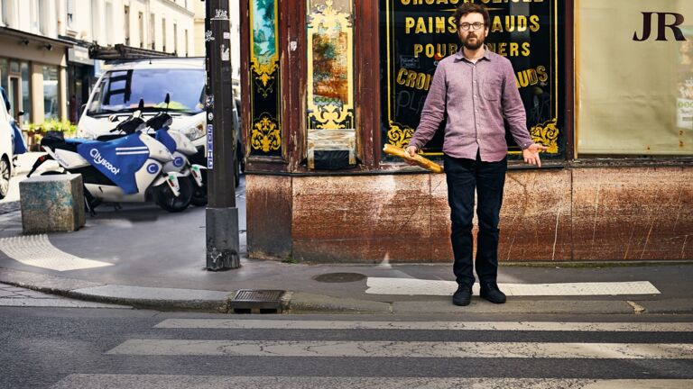 Was jetzt? Stehen oder gehen? Pierre Charrié wartet vor dem Bäcker auf Anweisungen des Fotografen. Immerhin hat er schon mal ganz stilecht ein Baguette in der Hand. Probiert hat er es offensichtlich bereits Pierre Charrié